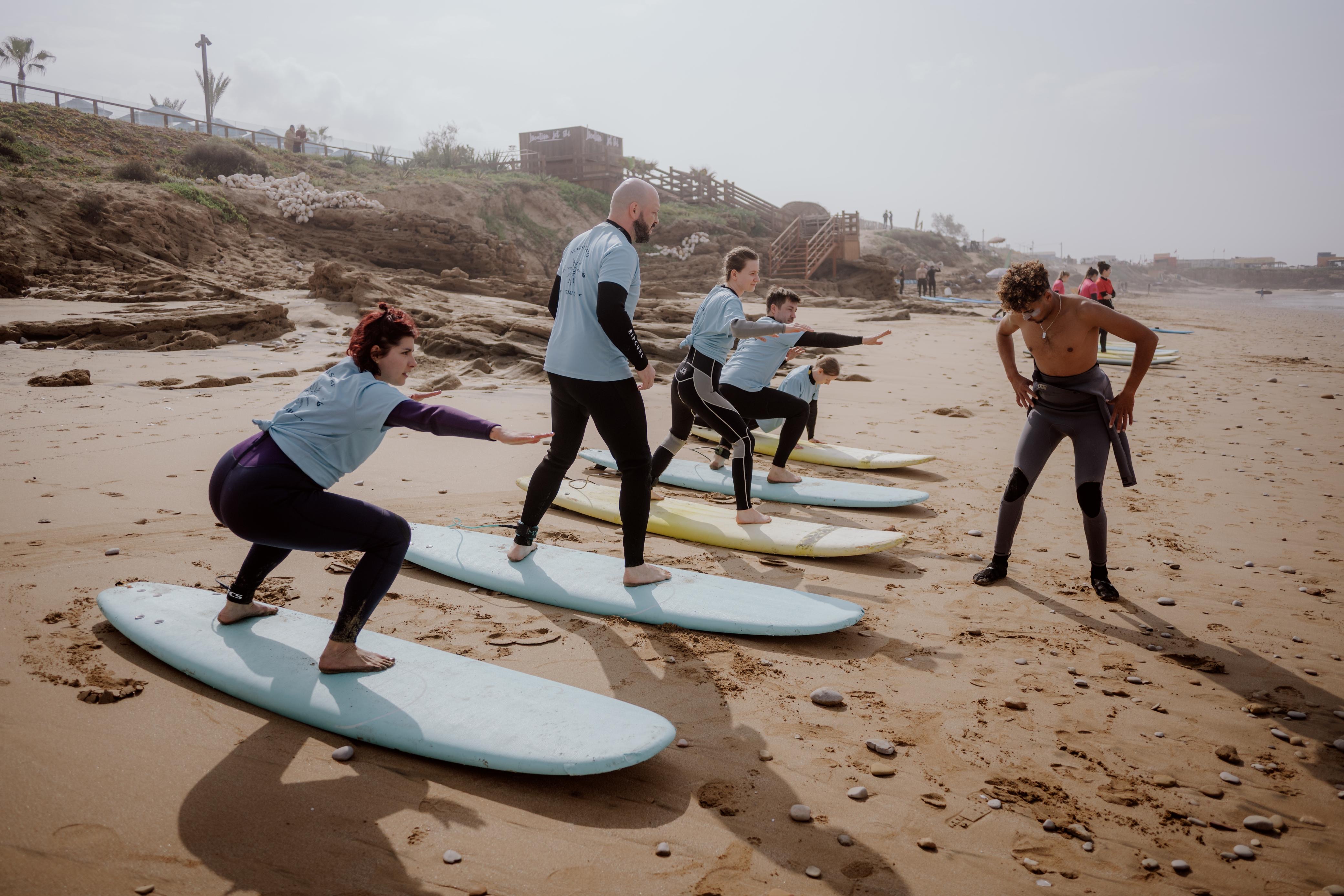 Students practising the pop-up on their boards on the beach while the coach watches